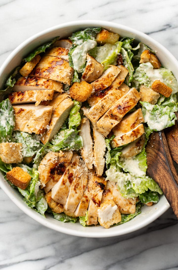 a bowl of cajun chicken caesar salad with salad utensils