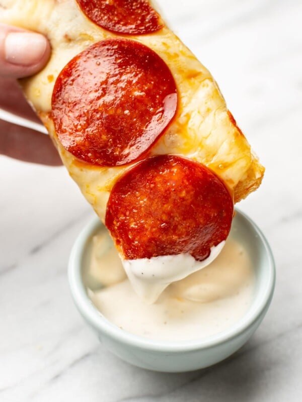 a hand dipping a slice of pepperoni french bread pizza in dip