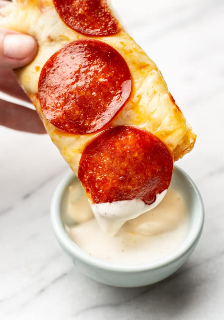 a hand dipping a slice of pepperoni french bread pizza in dip