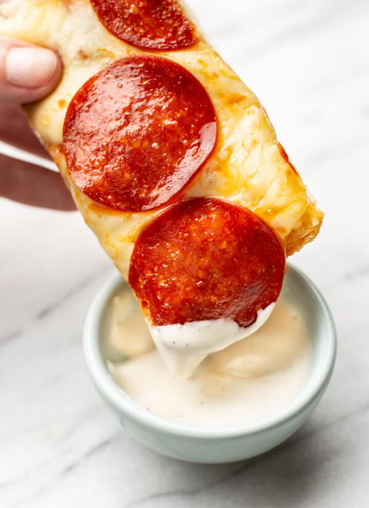 a hand dipping a slice of pepperoni french bread pizza in dip