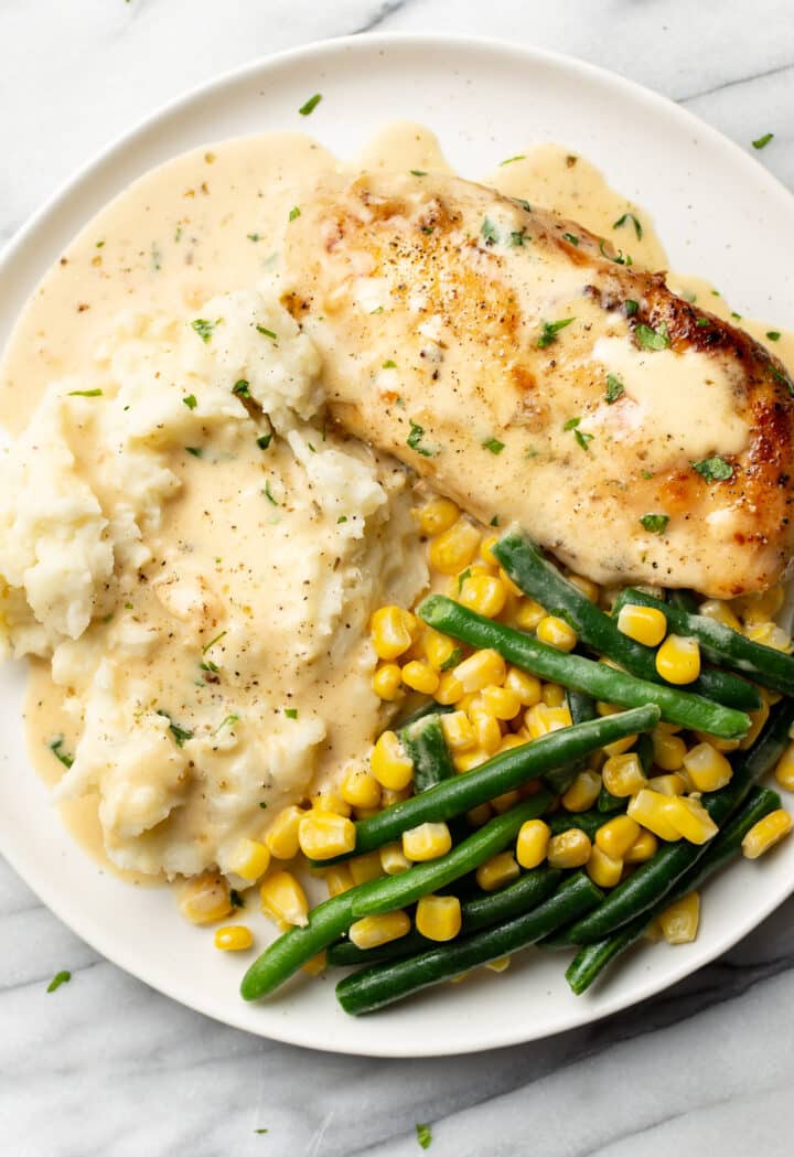 a plate with creamy white wine chicken, mashed potatoes, and green beans and corn