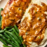 smothered chicken on a plate with mashed potatoes and green beans