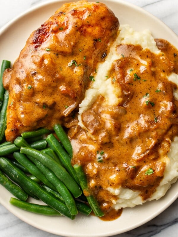 smothered chicken on a plate with mashed potatoes and green beans