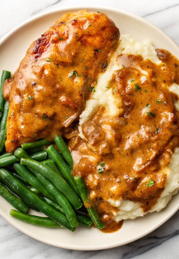 smothered chicken on a plate with mashed potatoes and green beans