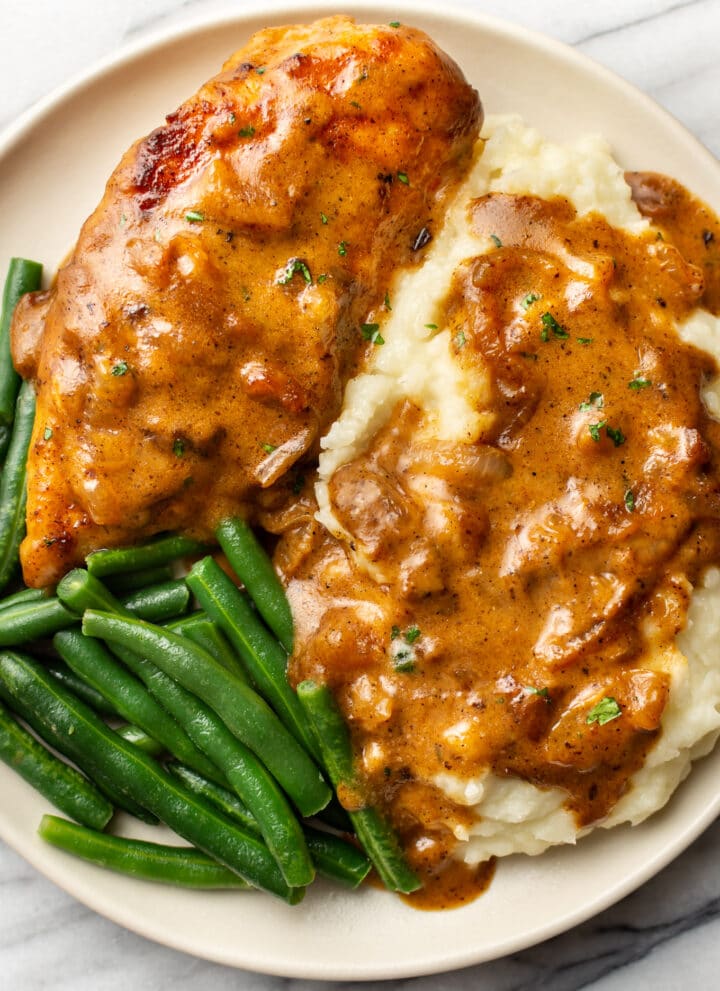 smothered chicken on a plate with mashed potatoes and green beans