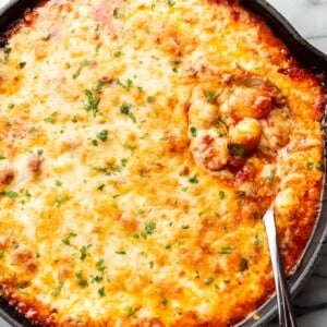 a cast iron skillet with baked gnocchi and a serving spoon