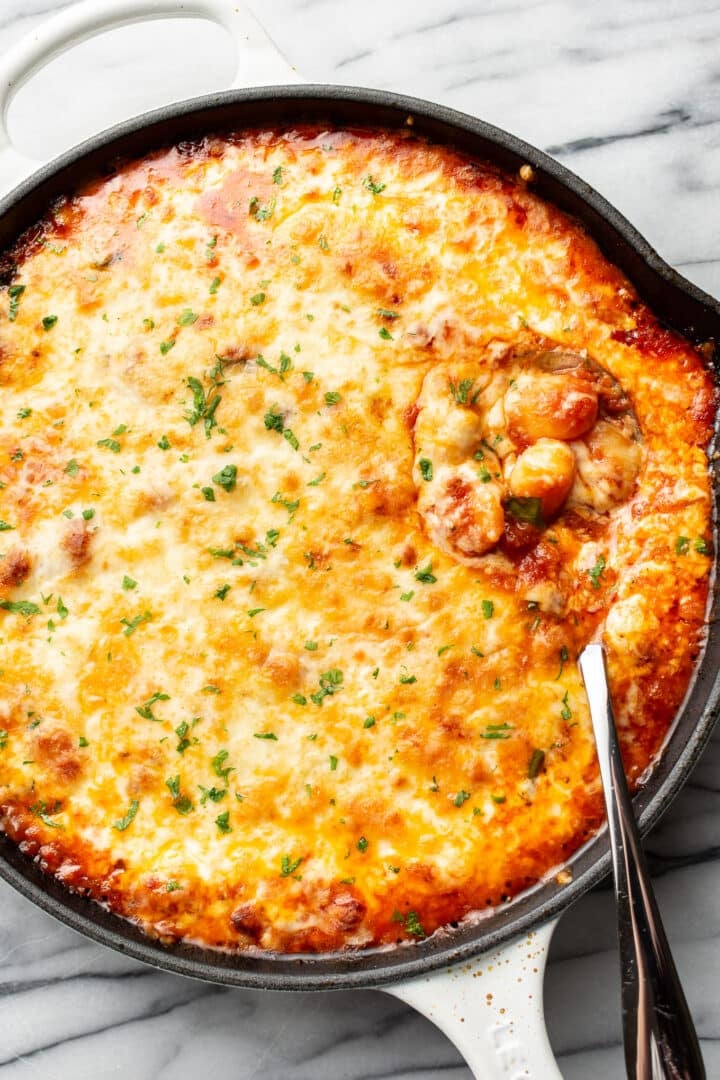 a cast iron skillet with baked gnocchi and a serving spoon