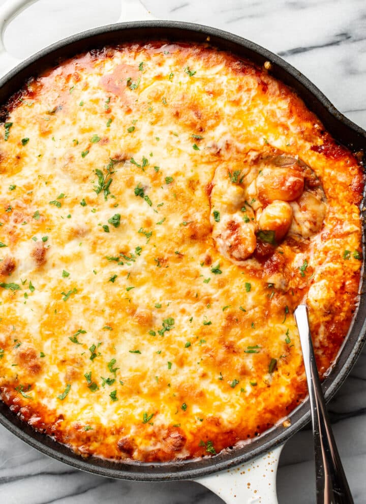 a cast iron skillet with baked gnocchi and a serving spoon