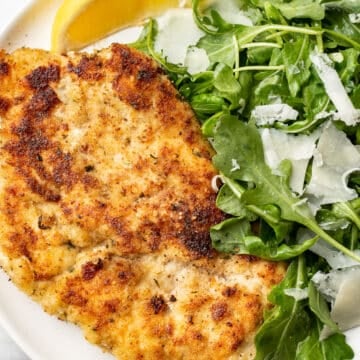 chicken milanese on a plate with arugula salad and a lemon wedge