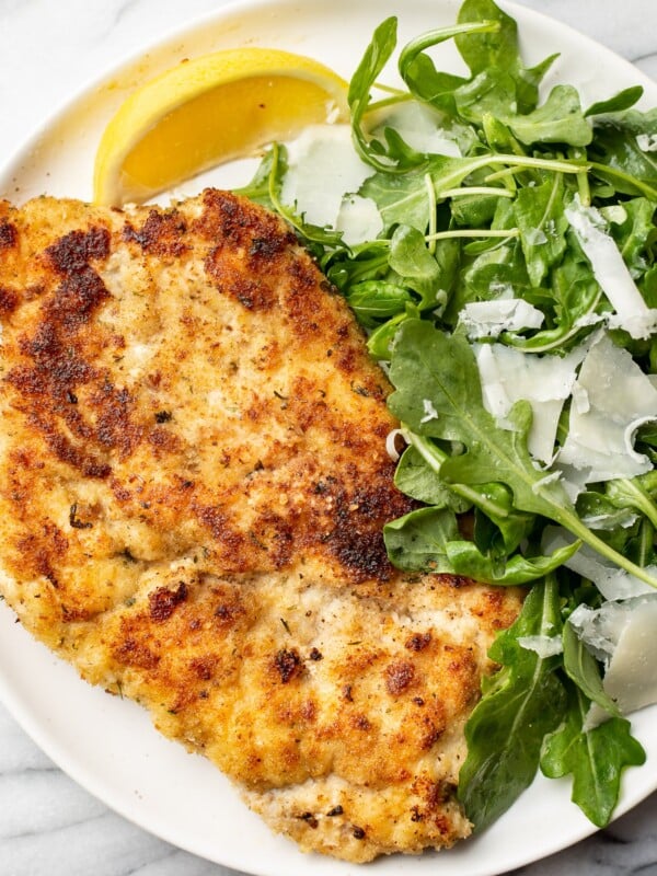 chicken milanese on a plate with arugula salad and a lemon wedge