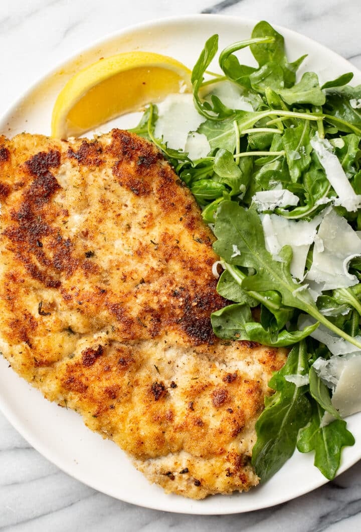 chicken milanese on a plate with arugula salad and a lemon wedge