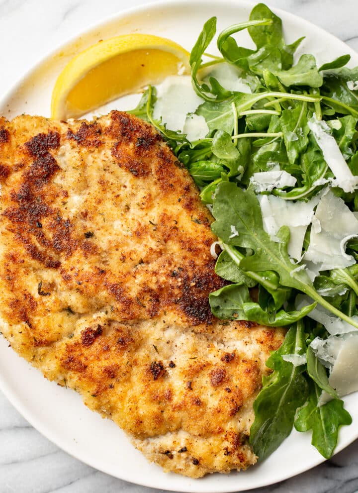 chicken milanese on a plate with arugula salad and a lemon wedge