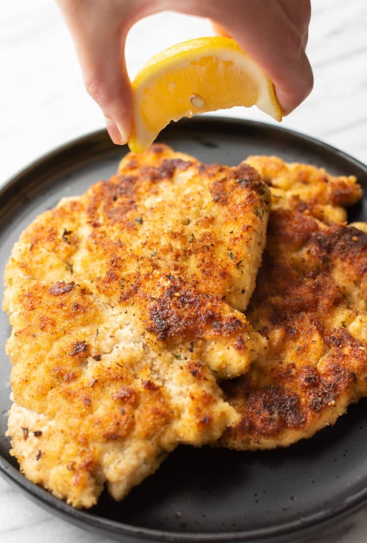 a hand squeezing lemon on chicken milanese