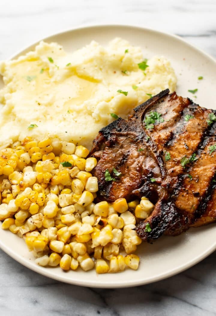 a plate with a grilled pork chop, corn, and mashed potatoes