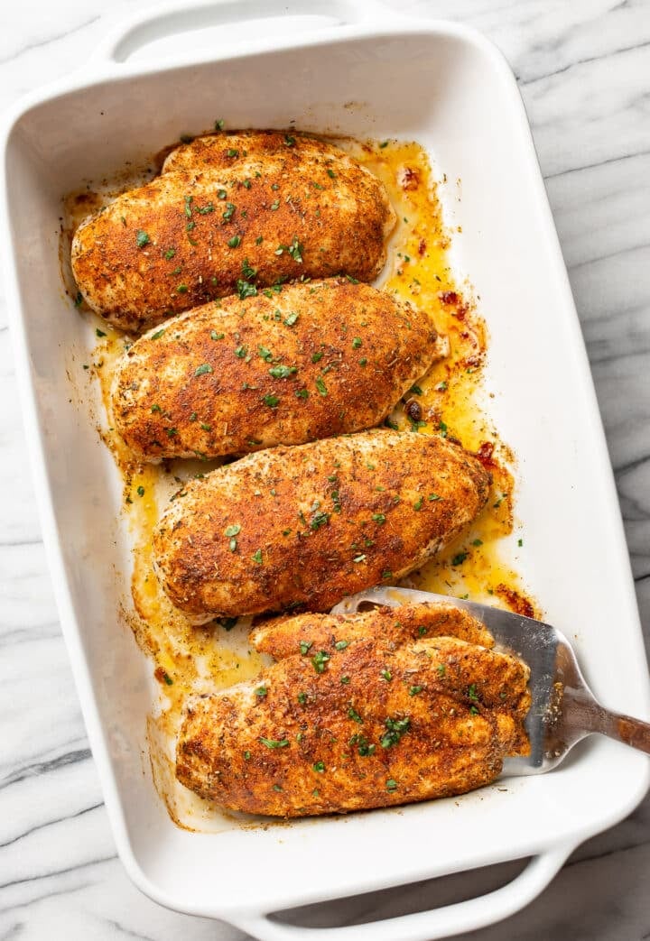 a casserole dish with baked chicken breast and a metal spatula