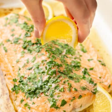 a hand squeezing lemon on baked salmon