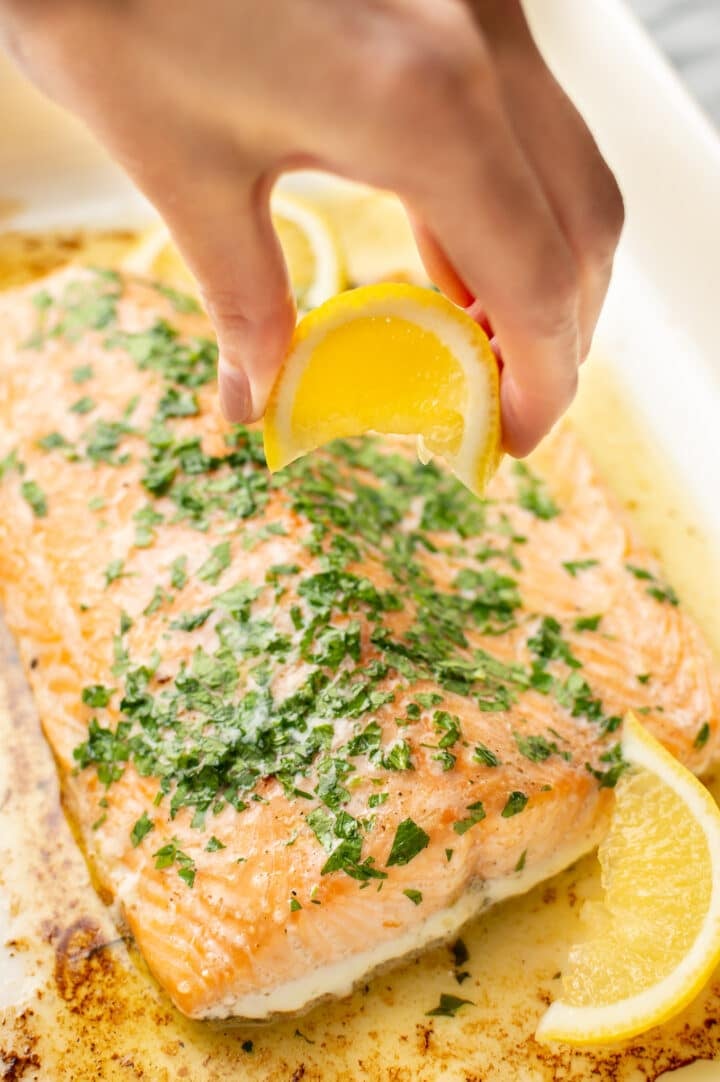 a hand squeezing lemon on baked salmon