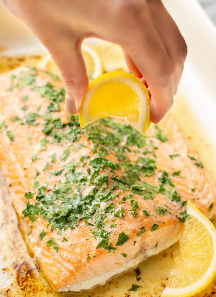 a hand squeezing lemon on baked salmon
