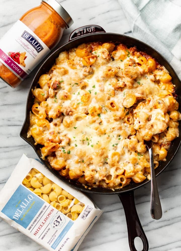 a skillet with spicy vodka pasta bake next to delallo products