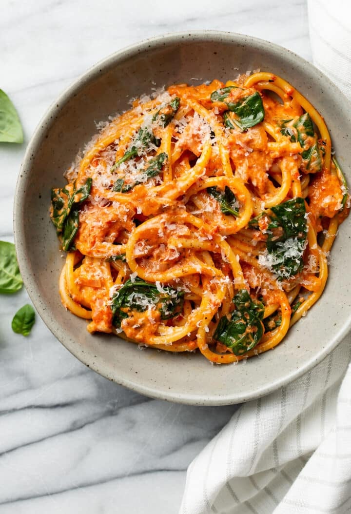 a bowl of roasted red pepper bucatini next to a cloth napkin