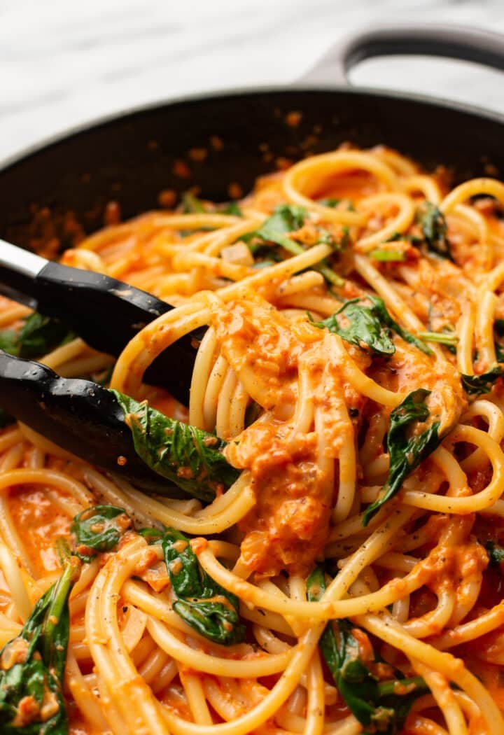 closeup of serving tongs in a skillet with roasted red pepper pasta