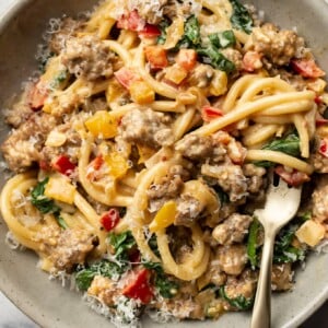 a bowl of creamy sausage and peppers pasta with a fork