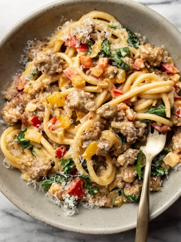 a bowl of creamy sausage and peppers pasta with a fork