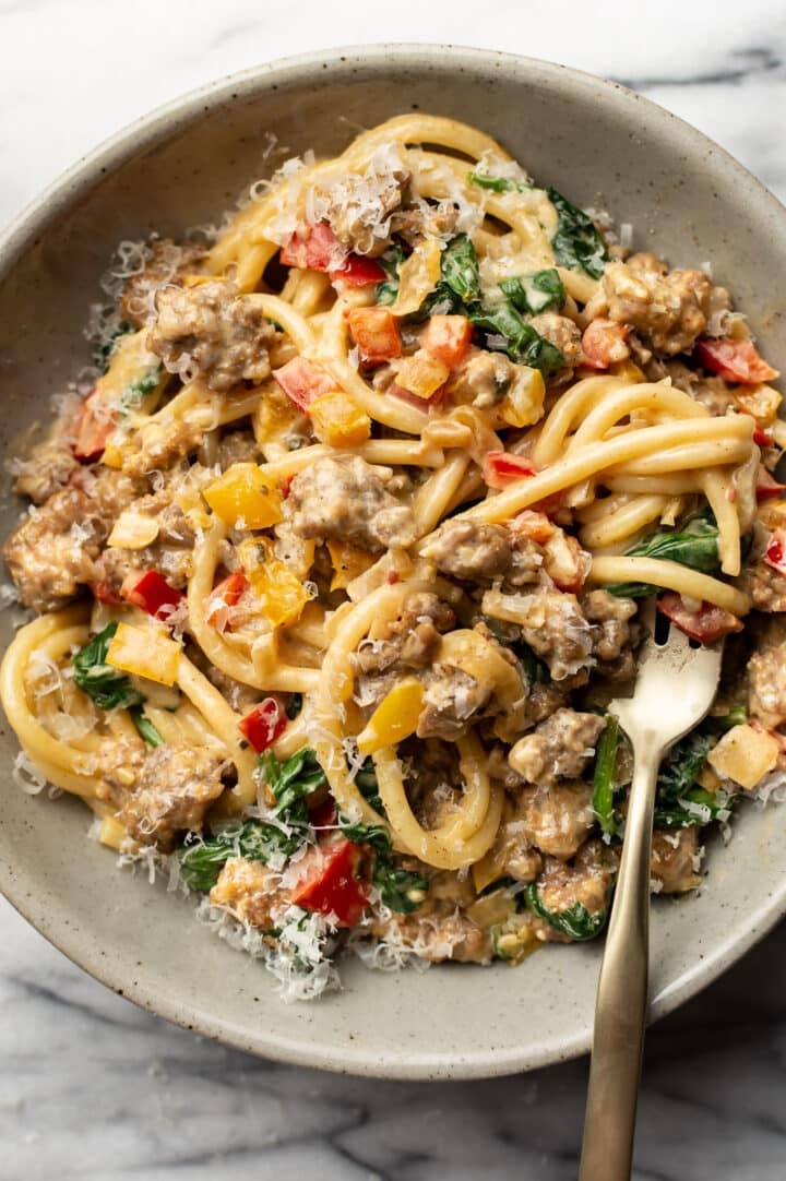 a bowl of creamy sausage and peppers pasta with a fork