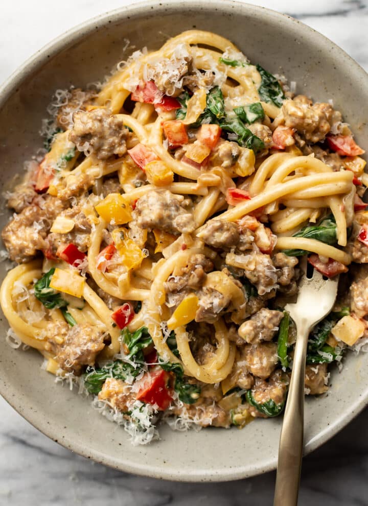 a bowl of creamy sausage and peppers pasta with a fork