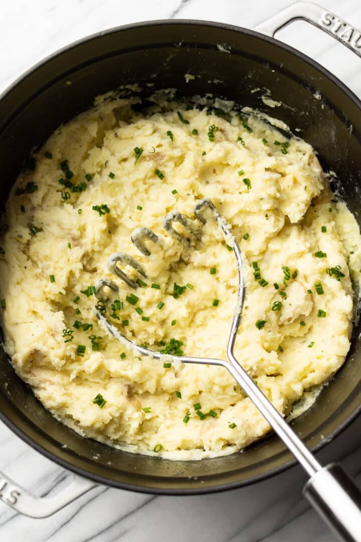 a pot of boursin mashed potatoes with a masher