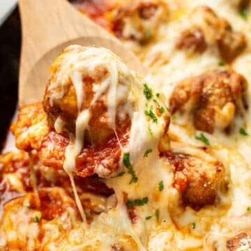 a wooden spoon with a cheese pull of chicken parmesan meatballs