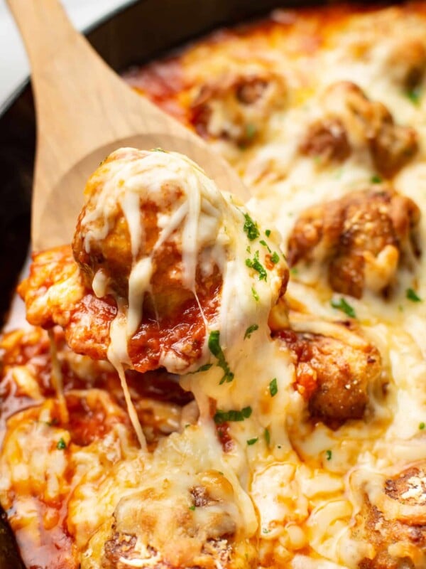 a wooden spoon with a cheese pull of chicken parmesan meatballs