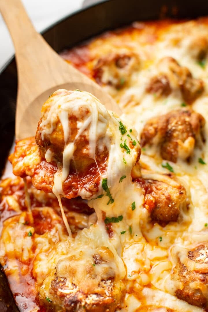 a wooden spoon with a cheese pull of chicken parmesan meatballs