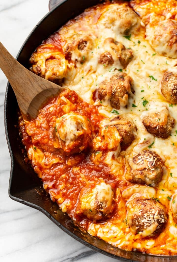closeup of a skillet of chicken parmesan meatballs with a wooden spoon