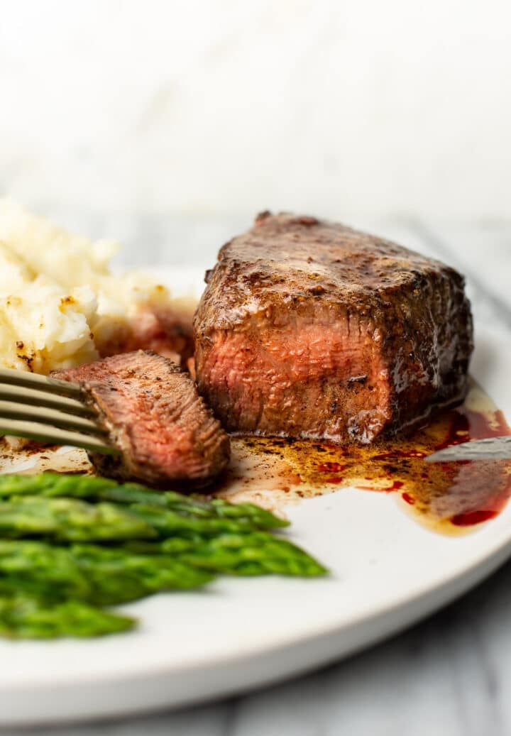 filet mignon on a plate with a fork, mashed potatoes, and asparagus