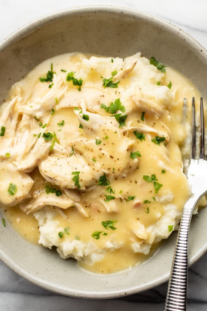 a bowl of shredded chicken and gravy over mashed potatoes