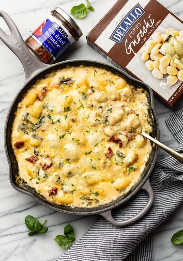 a skillet with tuscan baked gnocchi and a serving spoon