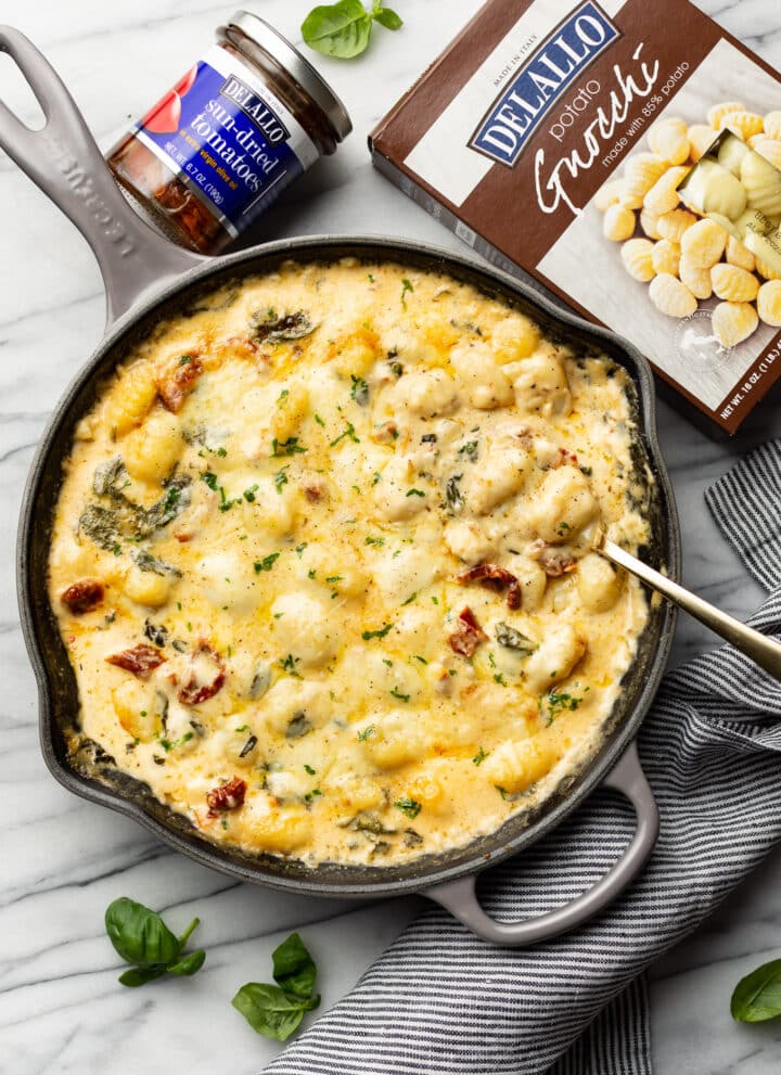 a skillet with tuscan baked gnocchi and a serving spoon
