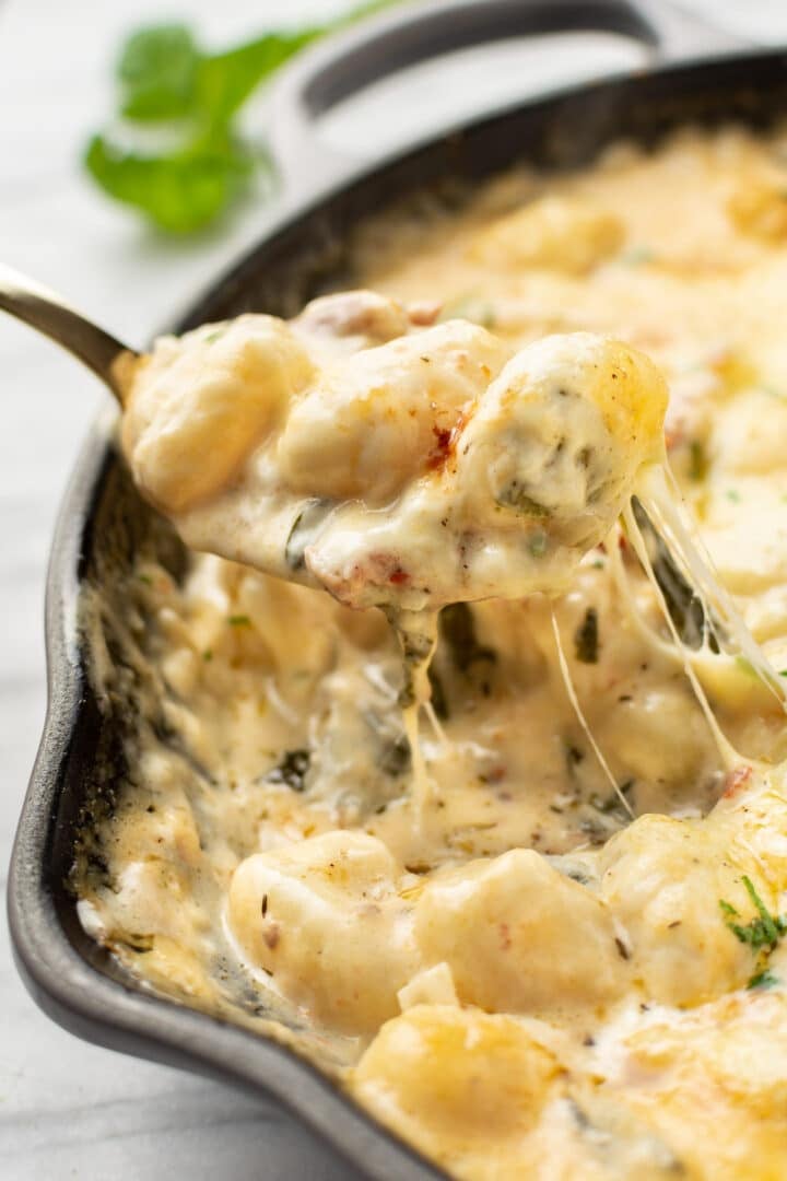 a closeup of a serving spoon over a skillet with tuscan baked gnocchi