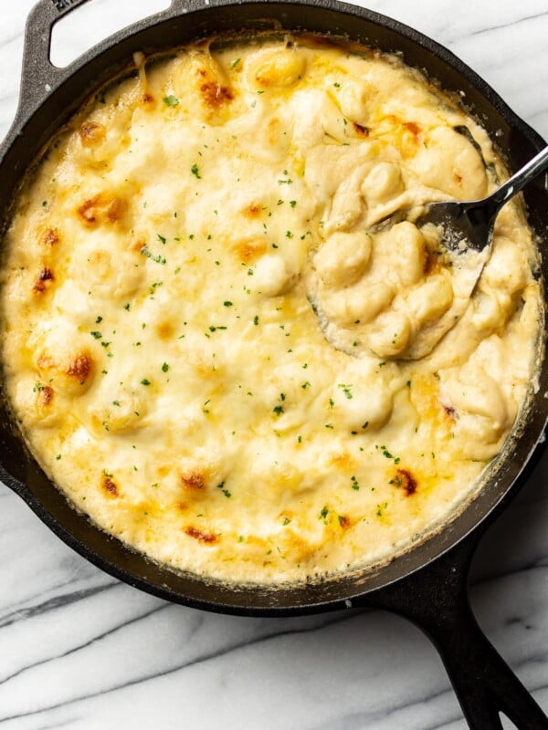 a skillet with cheesy gnocchi and a serving spoon