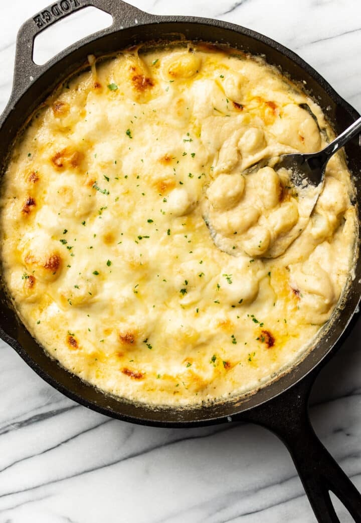 a skillet with cheesy gnocchi and a serving spoon