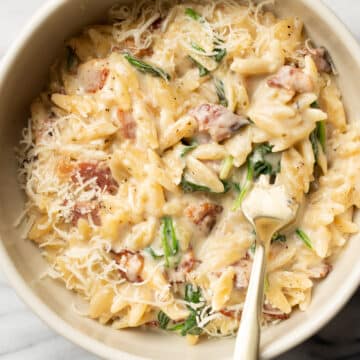 a bowl with spinach bacon orzo and a spoon