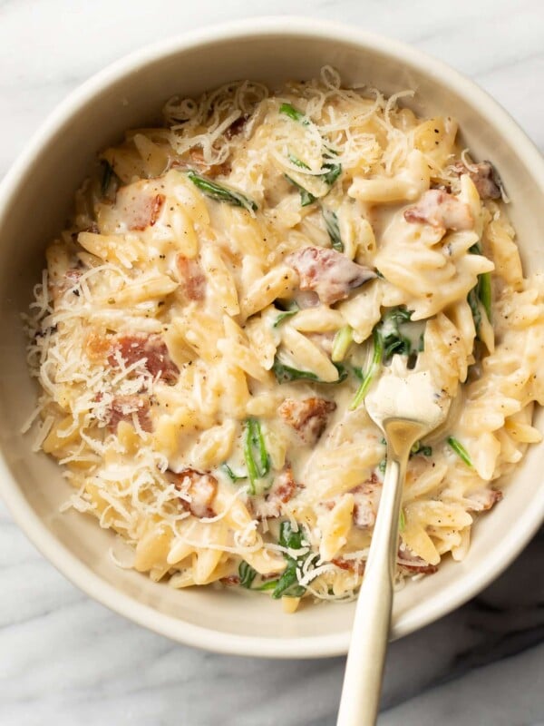 a bowl with spinach bacon orzo and a spoon