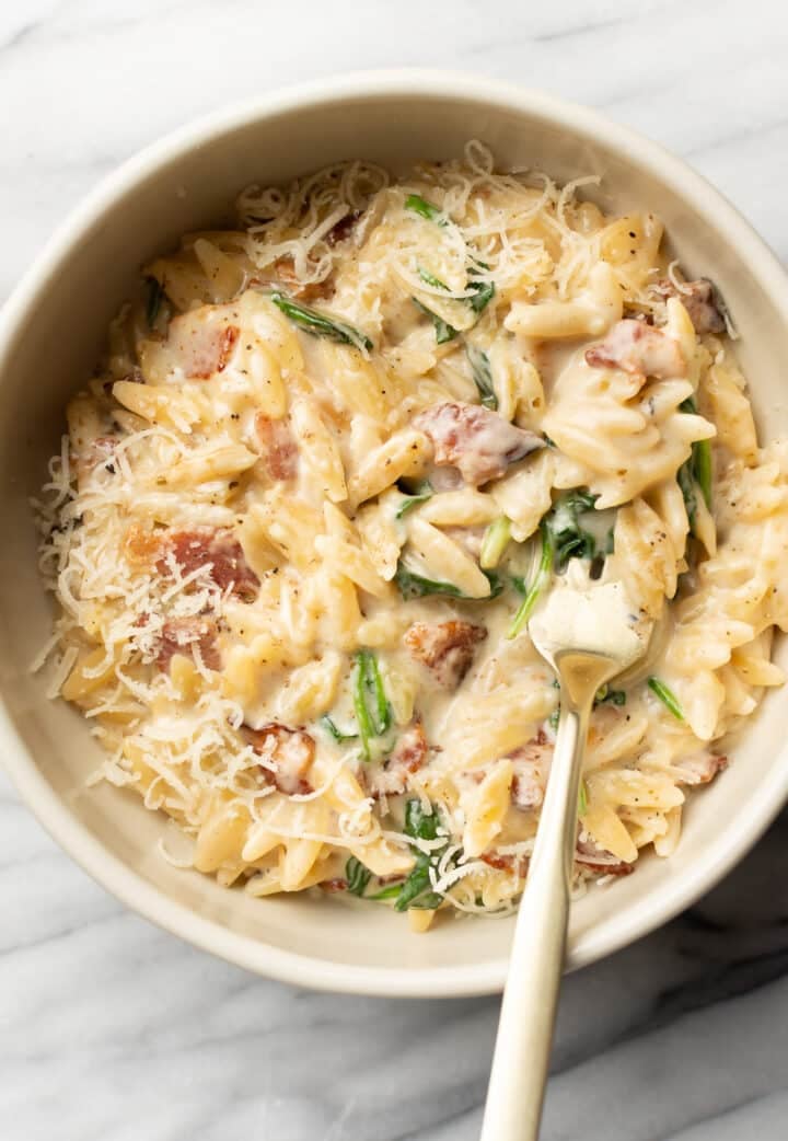a bowl with spinach bacon orzo and a spoon