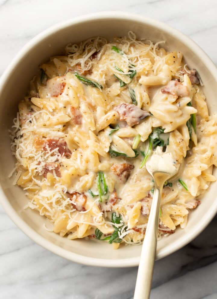 a bowl with spinach bacon orzo and a spoon