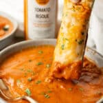 a piece of cheesy bread being dipped into zoup tomato bisque