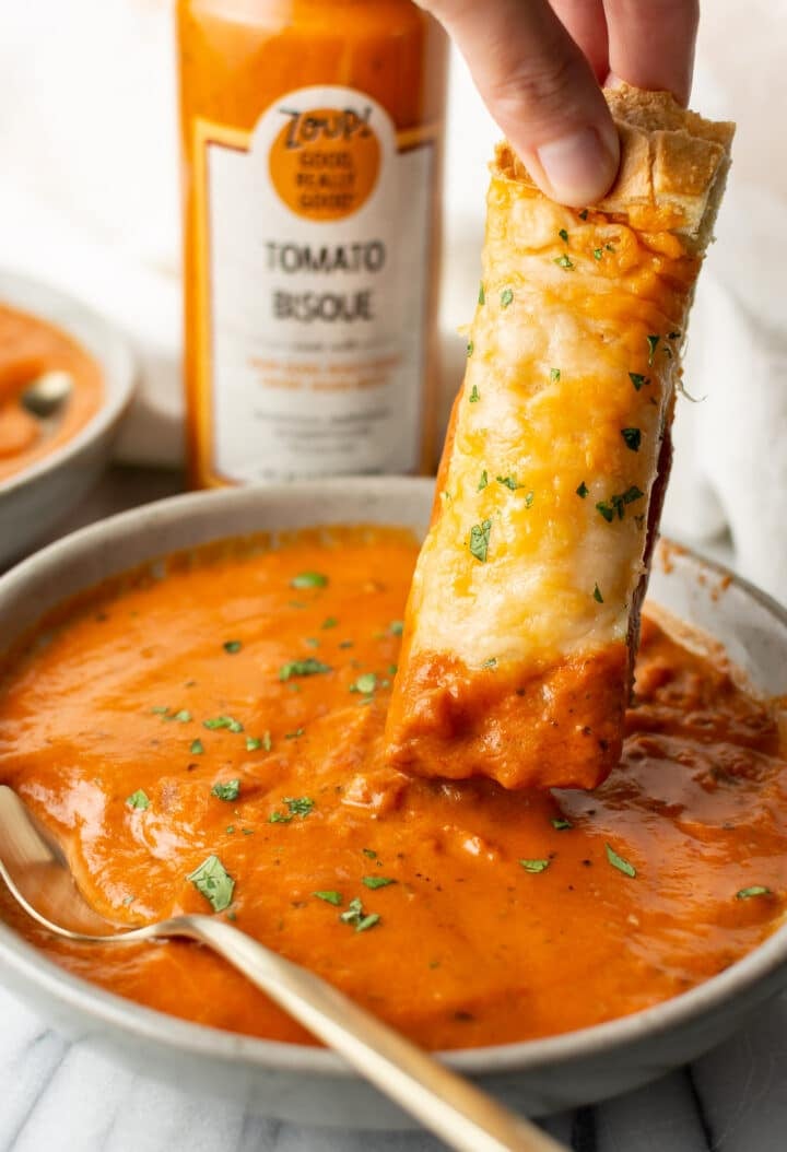 a piece of cheesy bread being dipped into zoup tomato bisque