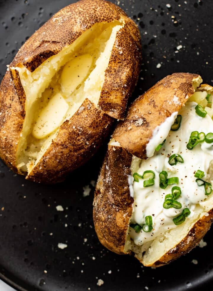 two baked potatoes on a plate with butter and sour cream