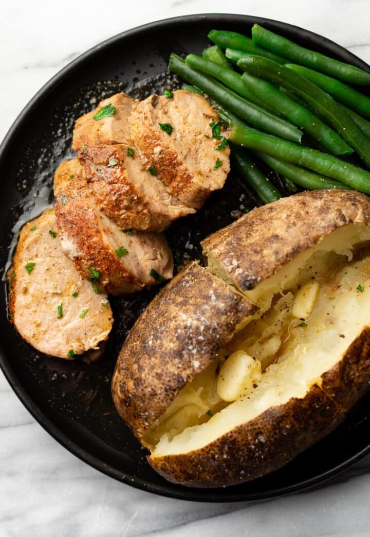 a plate with pork tenderloin, green beans, and a baked potato
