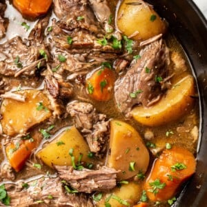 a dutch oven with pot roast beef, potatoes, and carrots